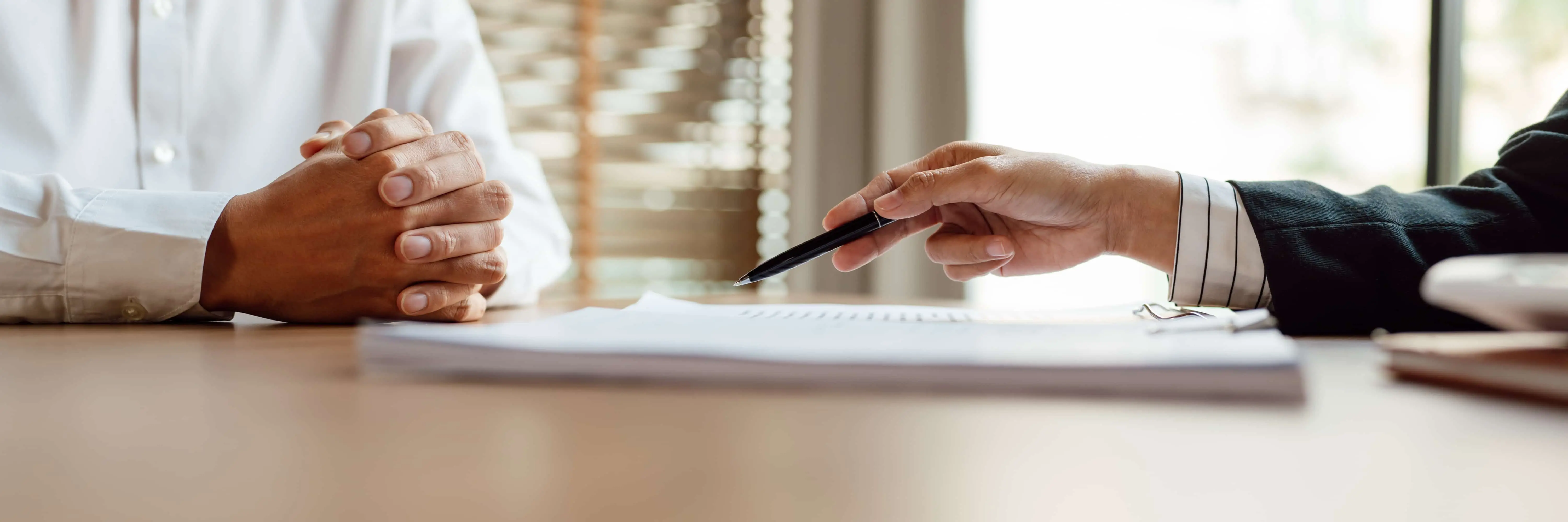 Two people seated across a desk with documents, one pointing to the paperwork with a pen.