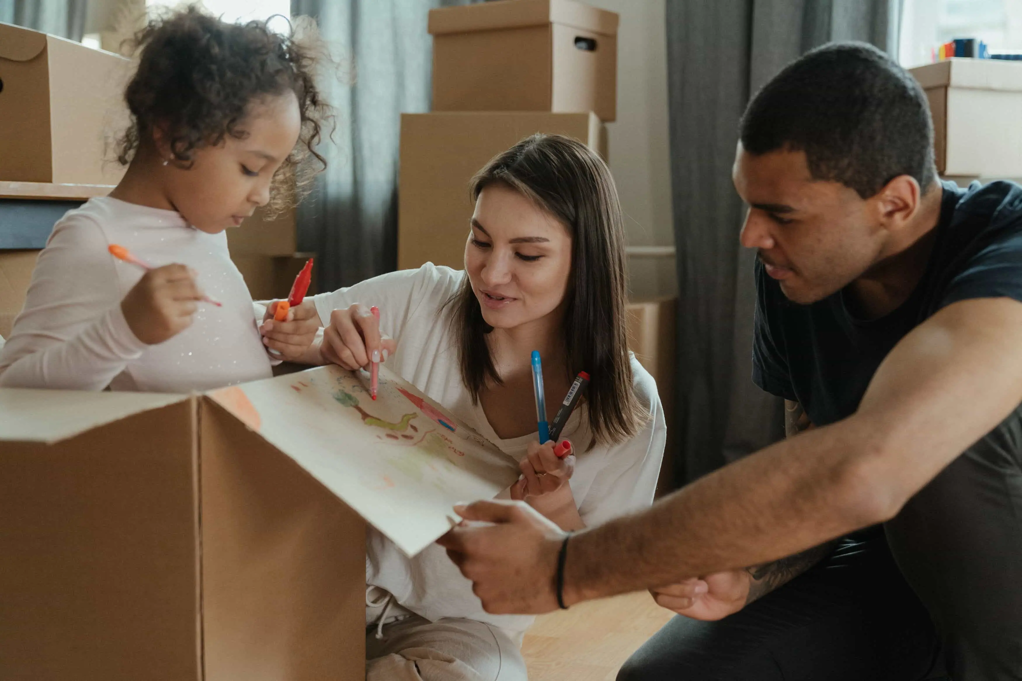 Parents and their daughter drawing on a cardboard moving box together.